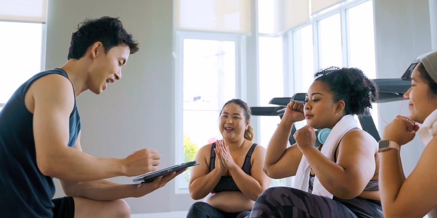 An instructor kneeling down opposite a group of women in a fitness class.