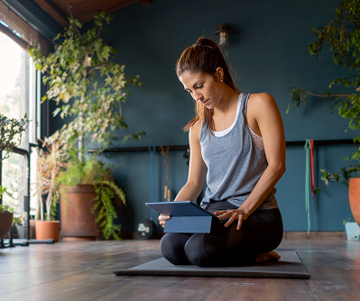 A yoga studio owner sits on a mat using a tablet, surrounded by natural light and plants—illustrating how modern studio owners manage their business digitally. Promotes the resource “How to manage your yoga studio using booking software,” highlighting the benefits of using Yoga Studio Management Software and Yoga Class Booking Software to streamline operations and improve member experience.